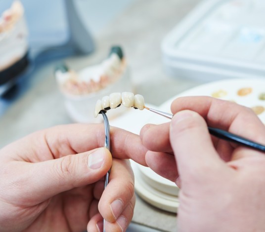 Zahntechniker bearbeitet mit einem Pinsel eine Zahnbrücke im Dentallabor.