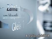 Milchglas-Tür mit der Aufschrift „Zahnärzte am Hauptbahnhof – Gleis 1“ in moderner Typografie.